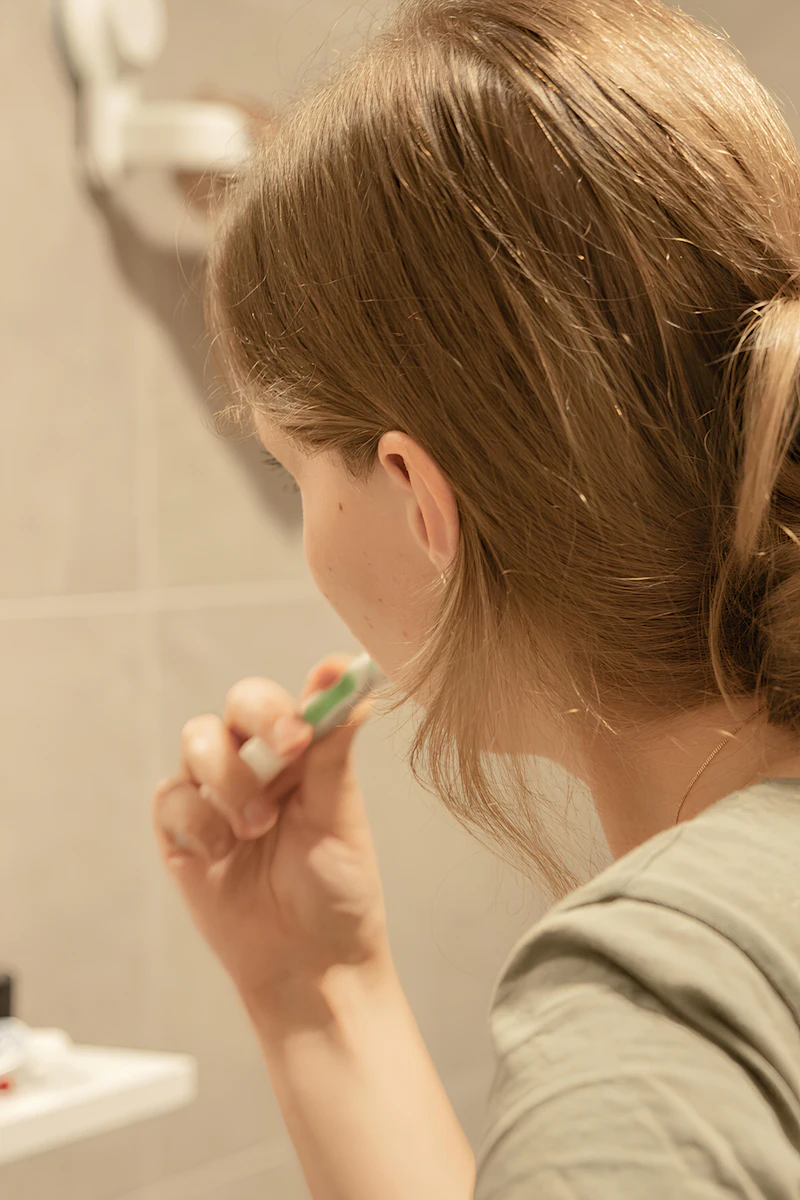 A woman brushing her teeth at the bathroom mirror in the morning